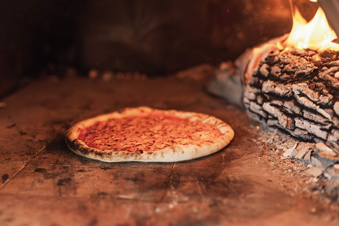 Pizza ao lado das brasas dentro do forno a lenha