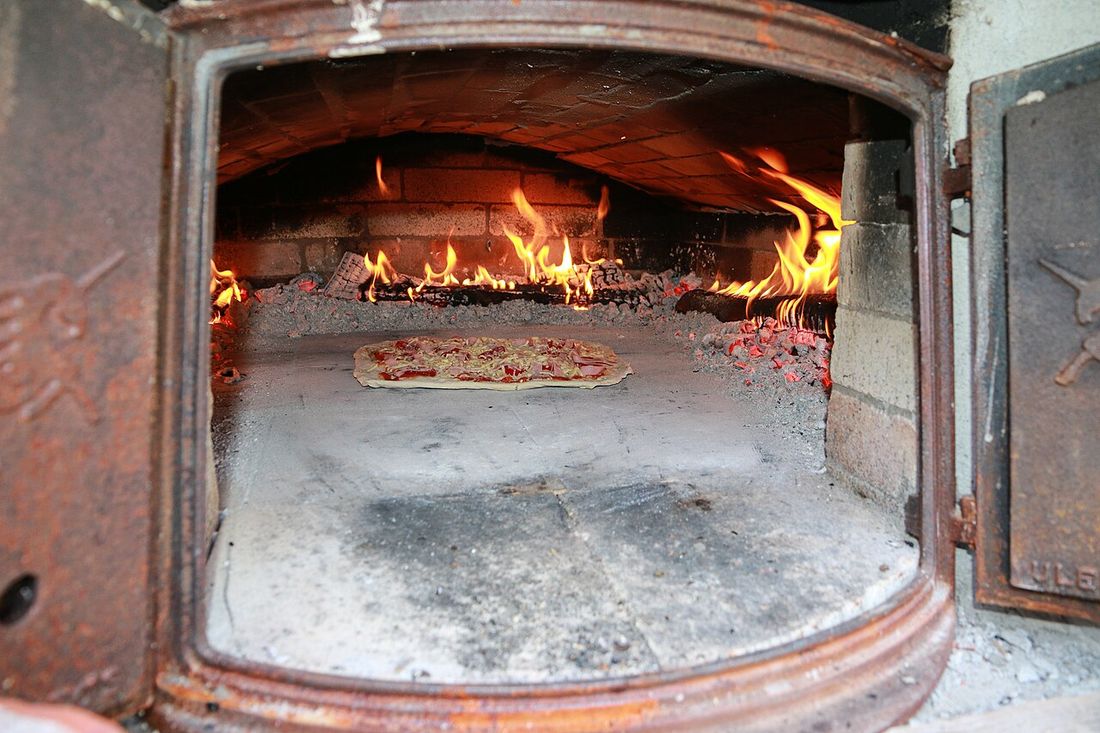 Pizza assando sobre o piso de pedra de um forno a lenha