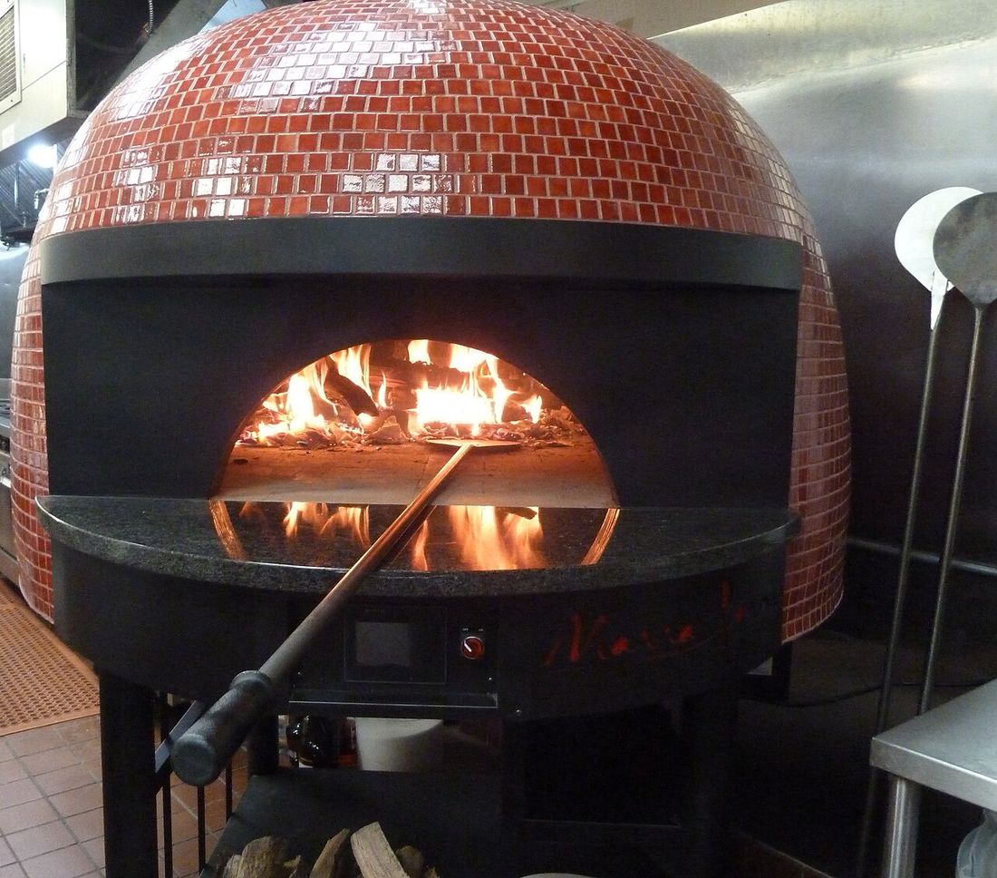 Forno de pizza em cúpula revestido de pastilhas vermelhas, com fogo aceso