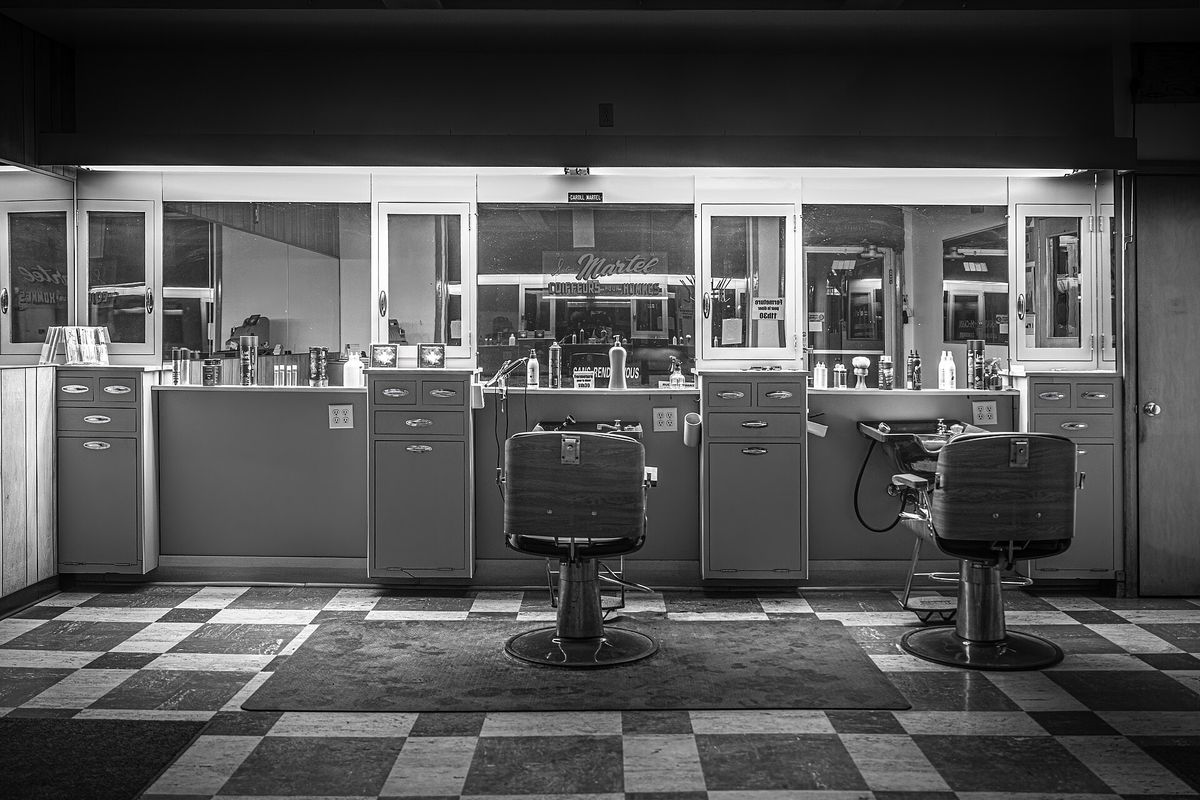 Salão de barbearia com duas cadeiras e piso quadriculado